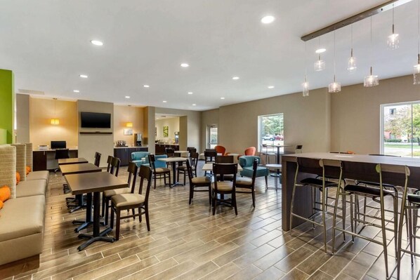 A modern hotel lobby with multiple seating areas, a bar, and a television screen.