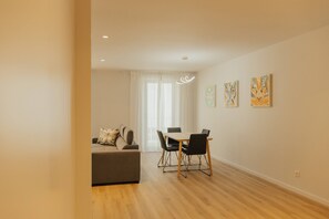 A modern living room with a sofa, dining table, and chairs, a window with curtains, and wall art.