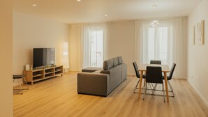Een moderne woonkamer met een bank, televisie, houten vloer en een eethoek met stoelen en een tafel.