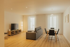 Un salon moderne avec un canapé, un téléviseur, un plancher en bois et un coin repas comprenant des chaises et une table.