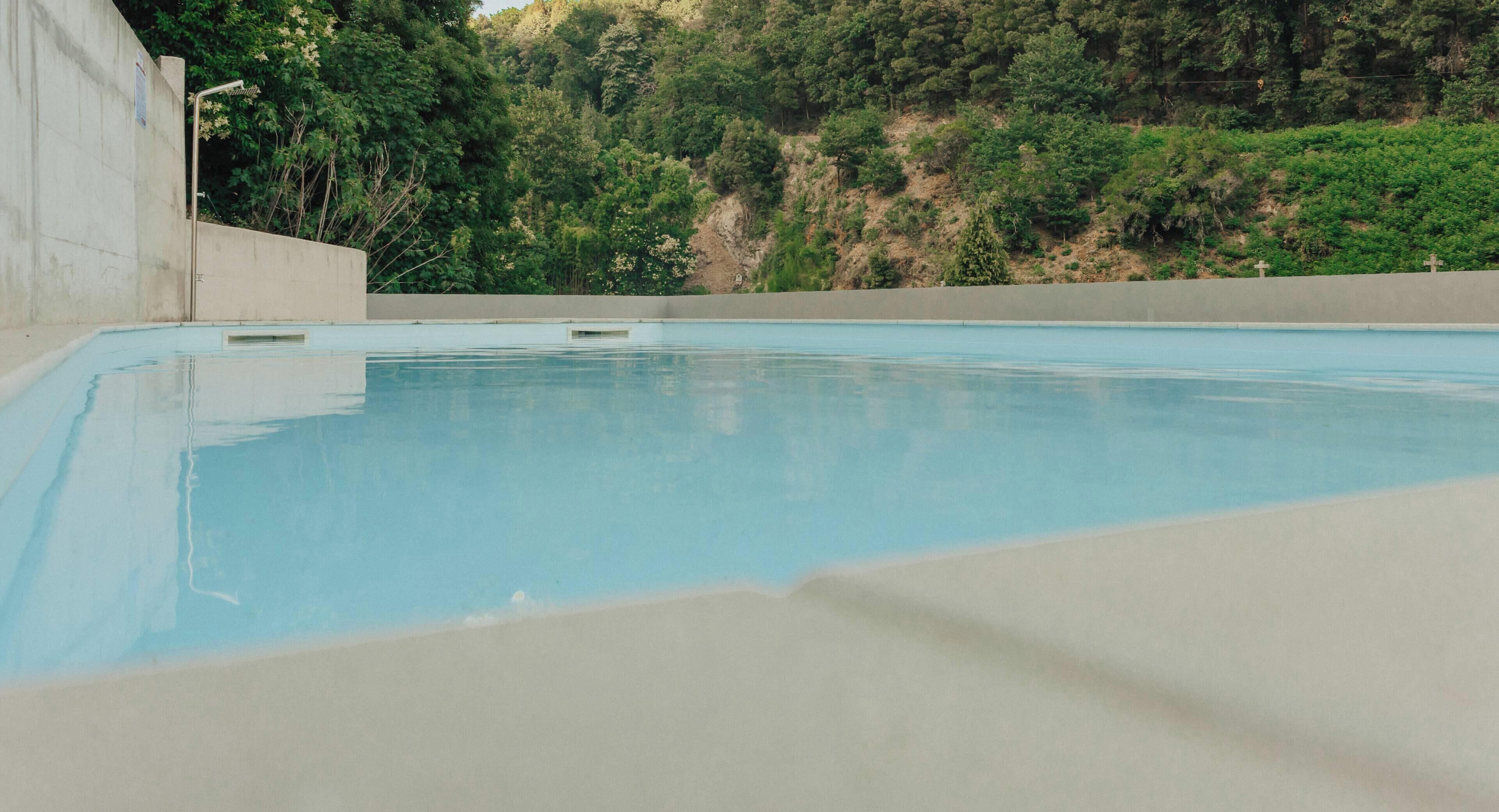 A swimming pool with a concrete edge and a view of a forested hillside in the background.