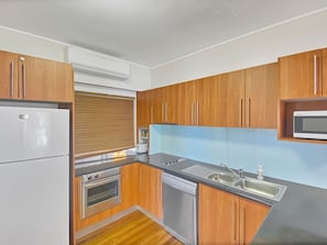 A compact kitchen with wooden cabinets, a built-in microwave, a stainless steel sink, and a dishwasher.