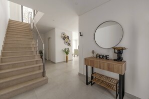 Un escalier menant à un palier, un miroir rond, une console sur laquelle est posé un objet décoratif portant l’inscription « HOME », et un élément décoratif mural.