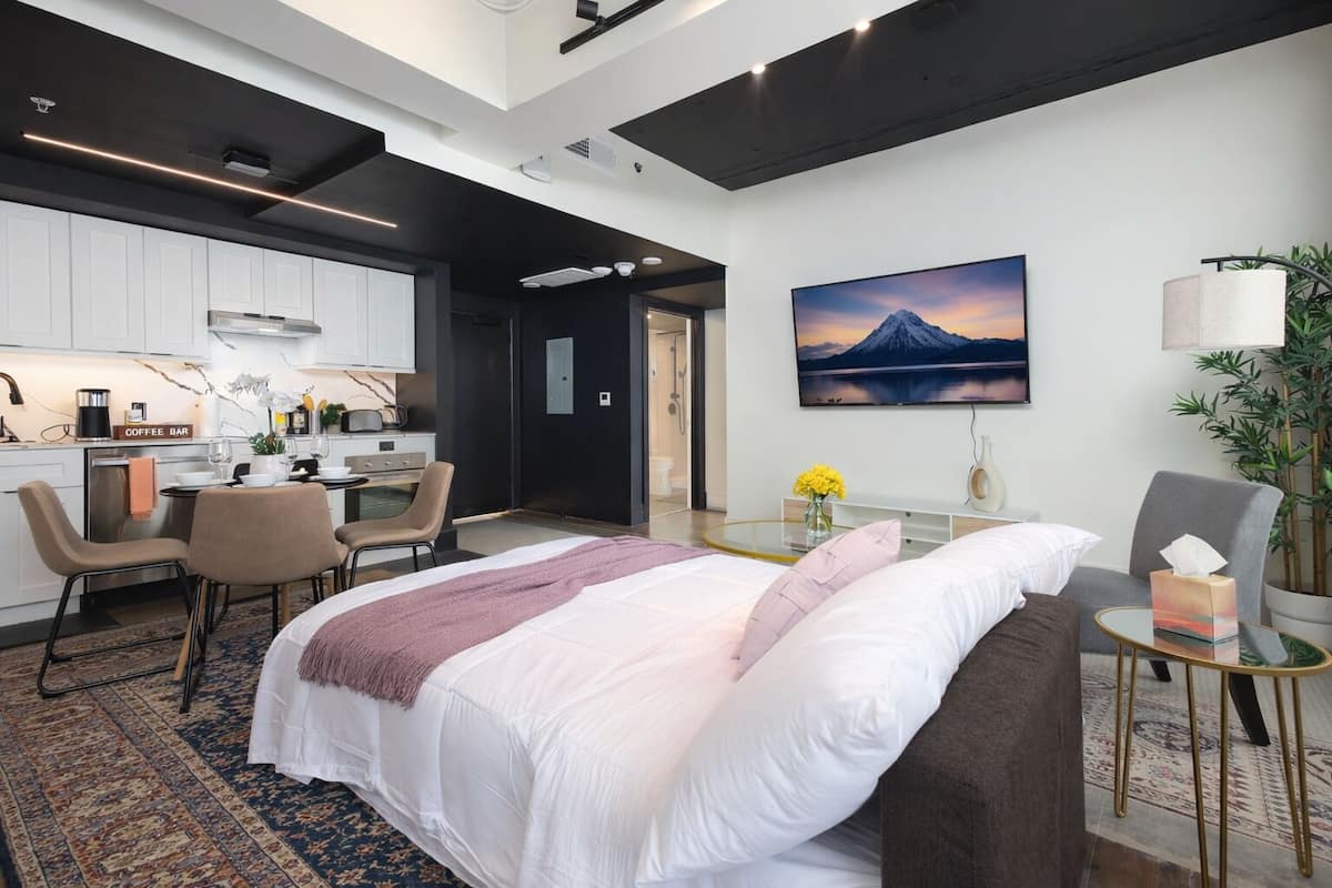 Una habitación de hotel moderna con una cama, un escritorio, una silla, una barra de café y un cuadro de una montaña.