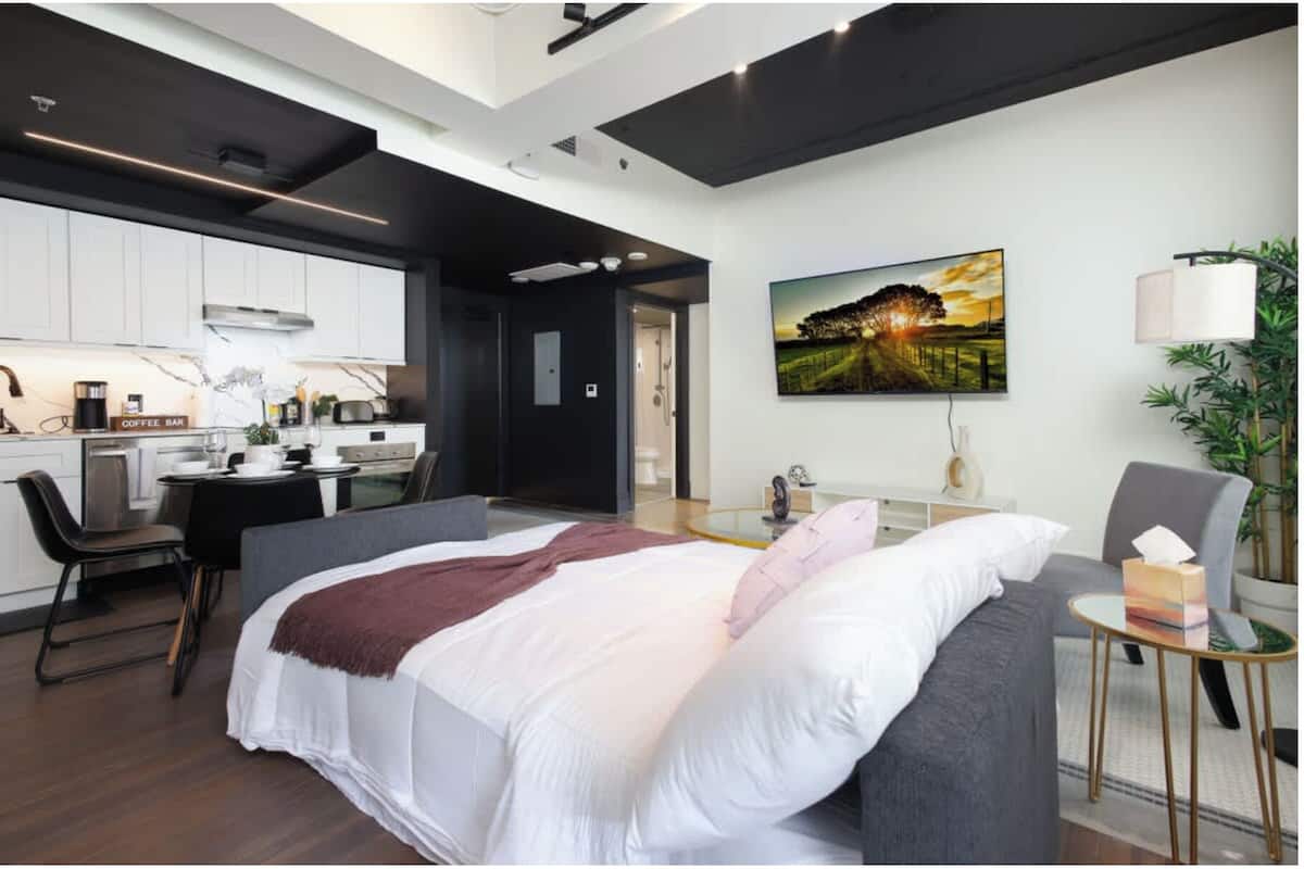 Una habitación de hotel moderna con una cama, un escritorio, una silla, una mesita, una lámpara y un cuadro en la pared.