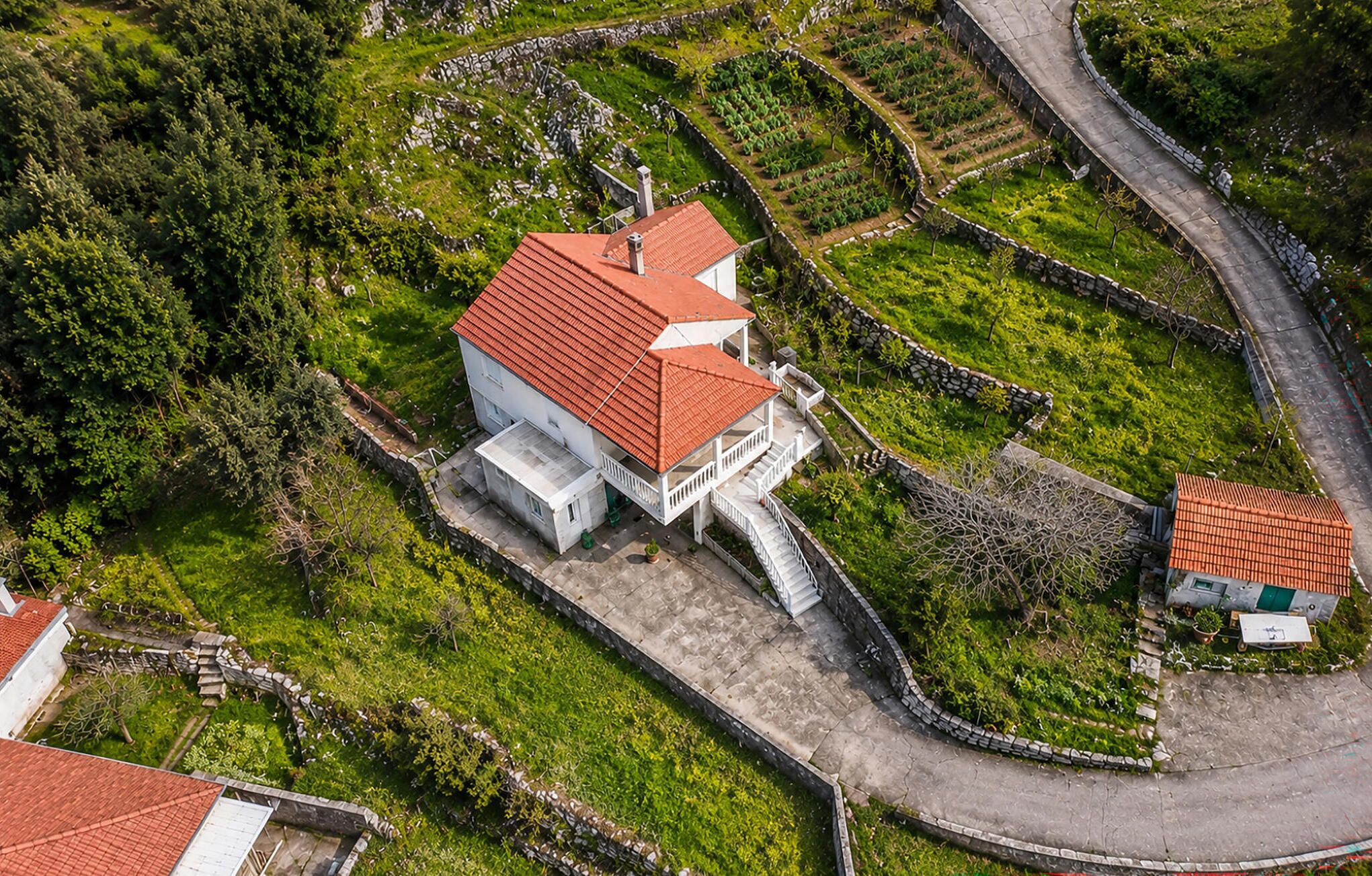 Une vue aérienne d’un bâtiment blanc surmonté d’un toit rouge, entouré de jardins en terrasses et d’un mur de pierre.