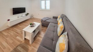 A living room with a grey sofa, a white coffee table, a flat-screen TV mounted on the wall, and a window with blinds. - Amazing home in Zrnovo with WiFi (Zrnovo)