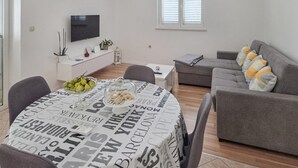 A modern living room with a grey sofa, a round table with a newspaper print tablecloth, and a TV mounted on the wall. - Amazing home in Zrnovo with WiFi (Zrnovo)