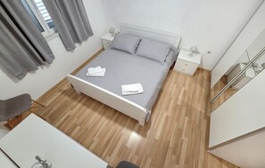 Una cama bien hecha con almohadas y toallas dobladas, una mesita de noche con lámpara y suelo de madera.