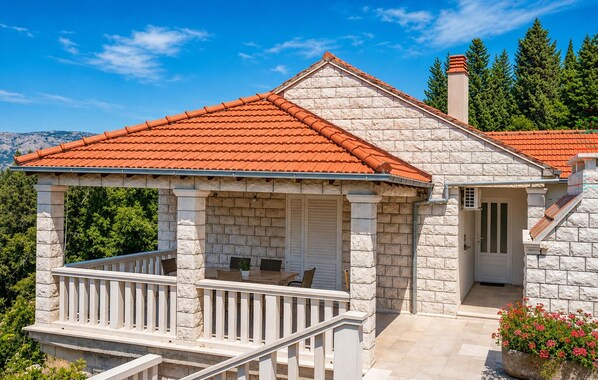 A stone building with a red-tiled roof, a covered porch with white railings, and a door leading to a covered entrance.