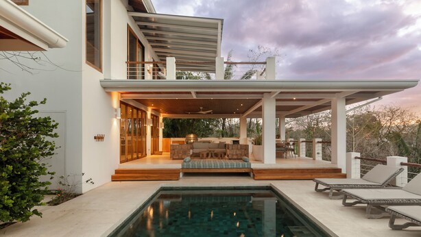 Ein modernes Haus mit Pool, Sitzgelegenheit im Freien und einer überdachten Terrasse.
