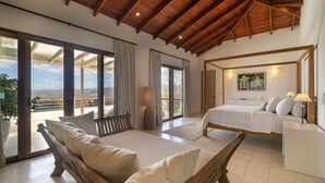 Ein Schlafzimmer mit Bett, einer Couch, einer hölzernen Bank, einem Gemälde und Blick ins Freie.