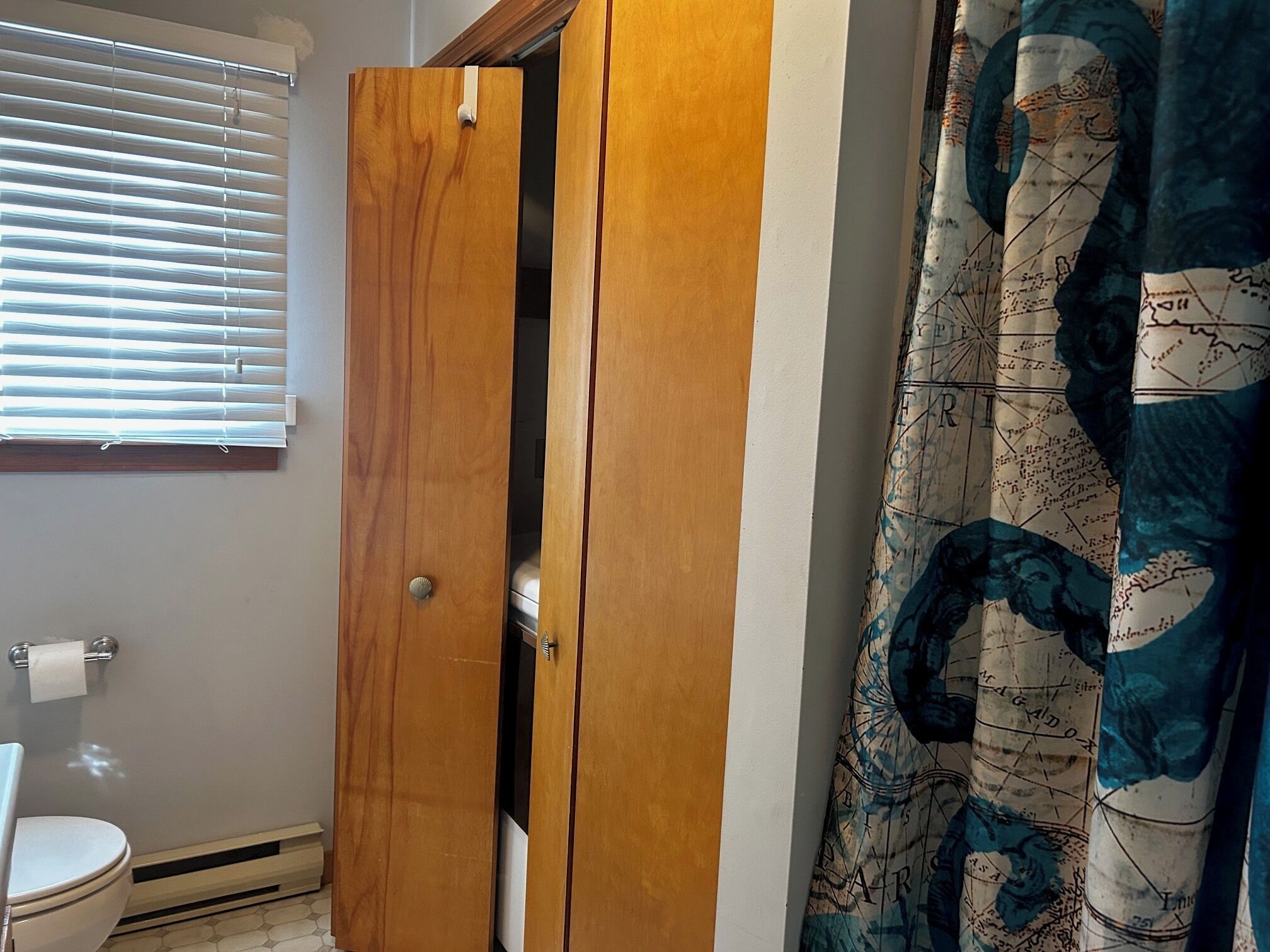 A wooden door in a bathroom with a toilet and a window with blinds.