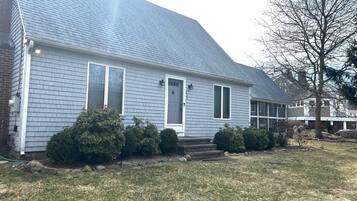 A single-story house with a grey shingle roof, a front door, and a small front yard with bushes and a lawn.