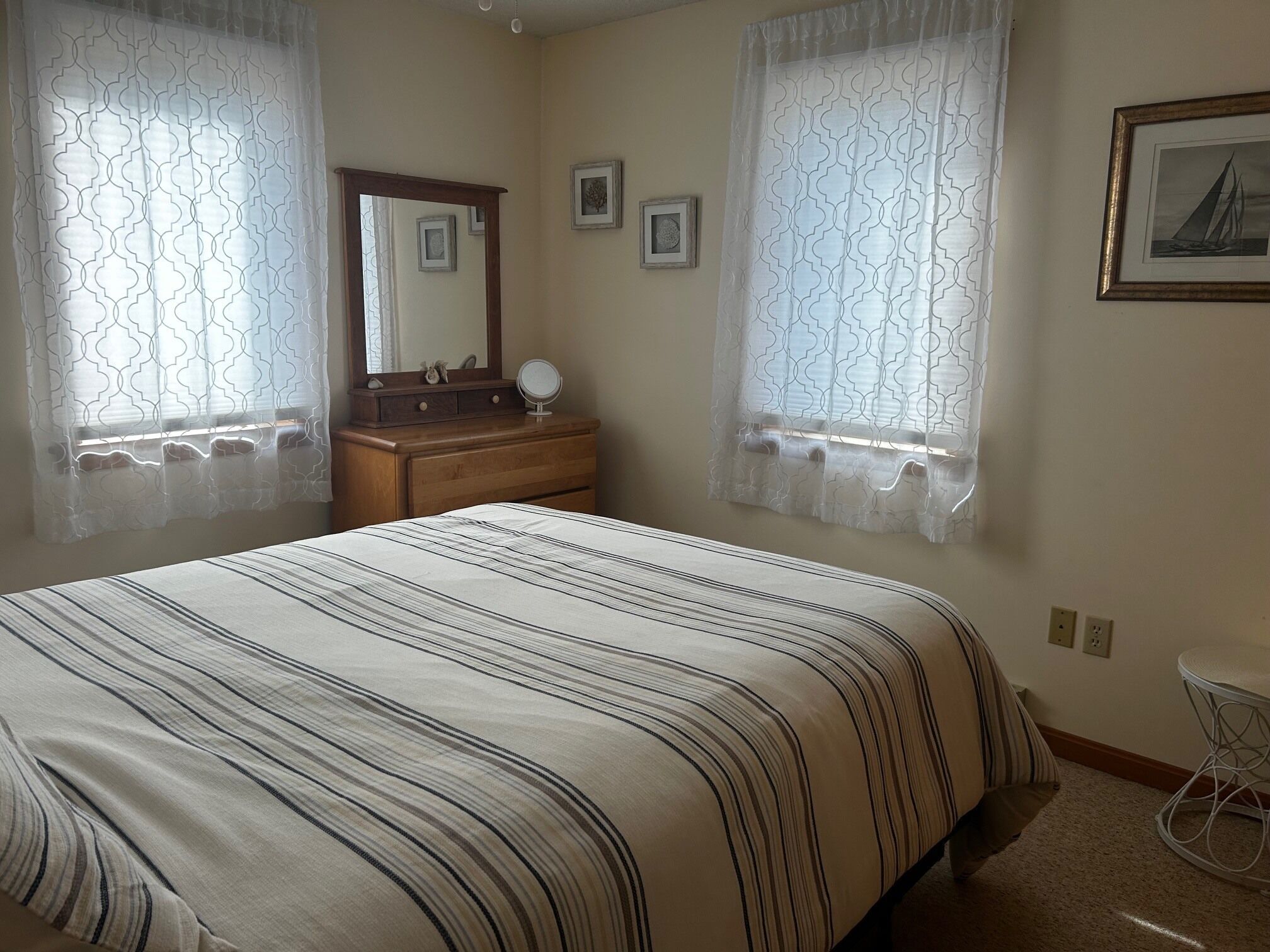 A bedroom with a bed, dresser, mirror, and two windows with patterned curtains.