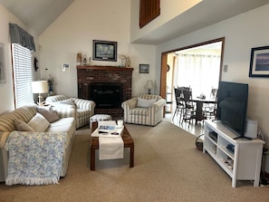 A living room with striped sofas, a fireplace, a television, and a dining area with a table and chairs. - Perfect 3-bedroom house in welcoming Green Hill Beach  neighborhood (South Kingstown)