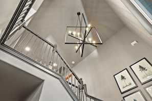 Eine Treppe mit einem modernen Kronleuchter und gerahmten Kunstwerken an den Wänden.