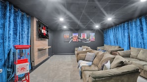 Un cine en casa con una pantalla grande, una máquina de palomitas y tres carteles de películas en la pared.