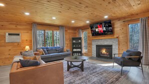 Ein gemütliches Blockhaus-Interieur mit Kamin, einer Couch, einem Couchtisch und einem an der Wand befestigten Fernseher.
