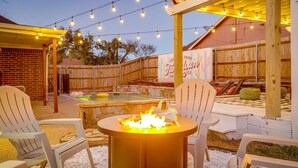 Eine Terrasse im Freien mit Feuerschale, Lichterkette und Holzlattenzaun.