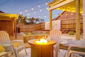 Une terrasse extérieure avec un foyer, des guirlandes lumineuses et une clôture en bois.