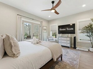 A bedroom with a bed, a ceiling fan, a TV, a dresser, and a window with a view.
