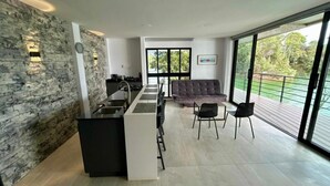 Una cocina moderna con un muro de acento de piedra, una zona de comedor con sofá y sillas, y un ventanal con vistas a la vegetación.