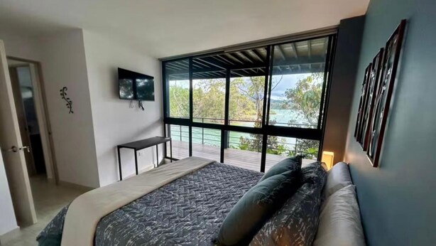 Un dormitorio con cama, televisor, escritorio y balcón con vistas.