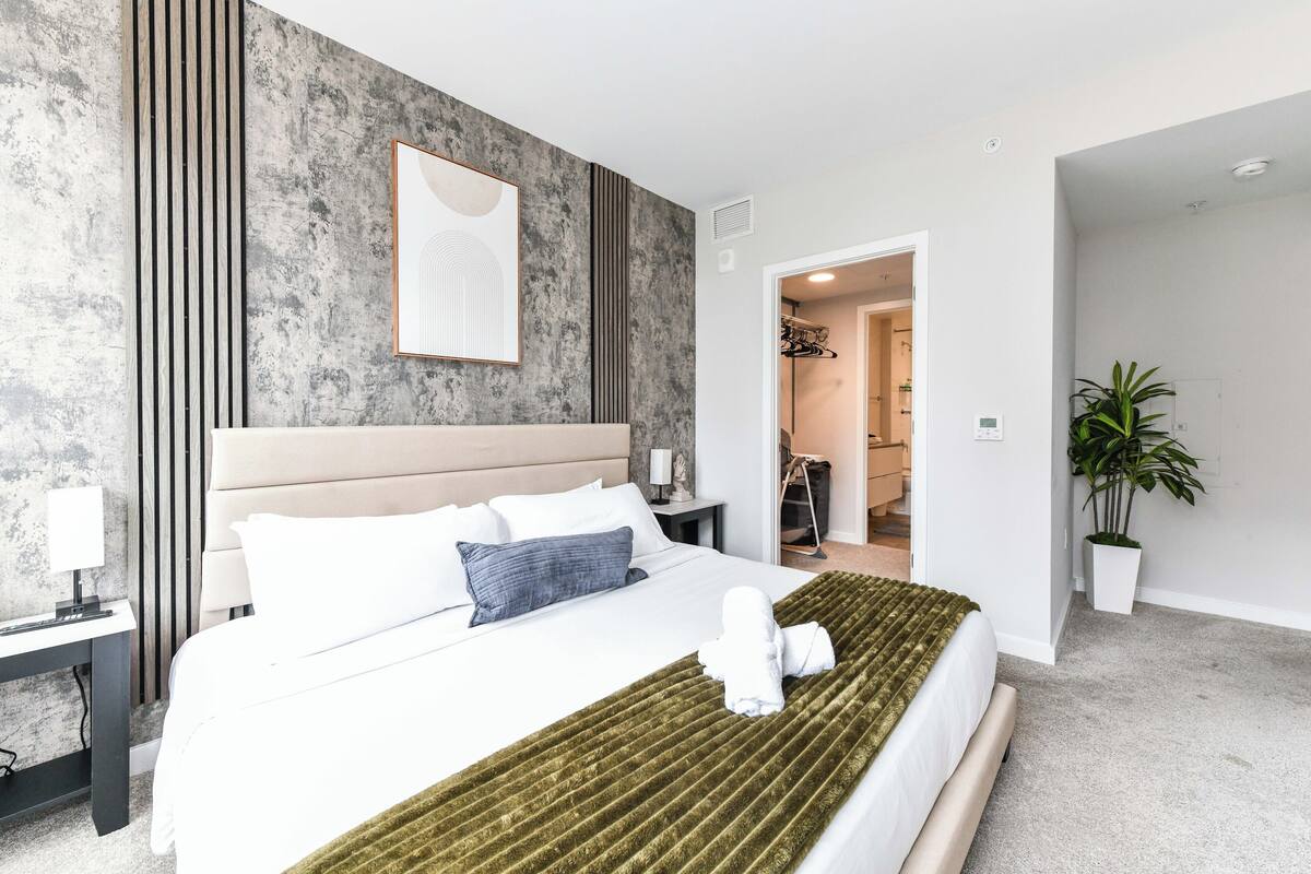Une chambre d’hôtel moderne avec un grand lit, une table de chevet, une œuvre d’art accrochée au mur et une plante en pot.