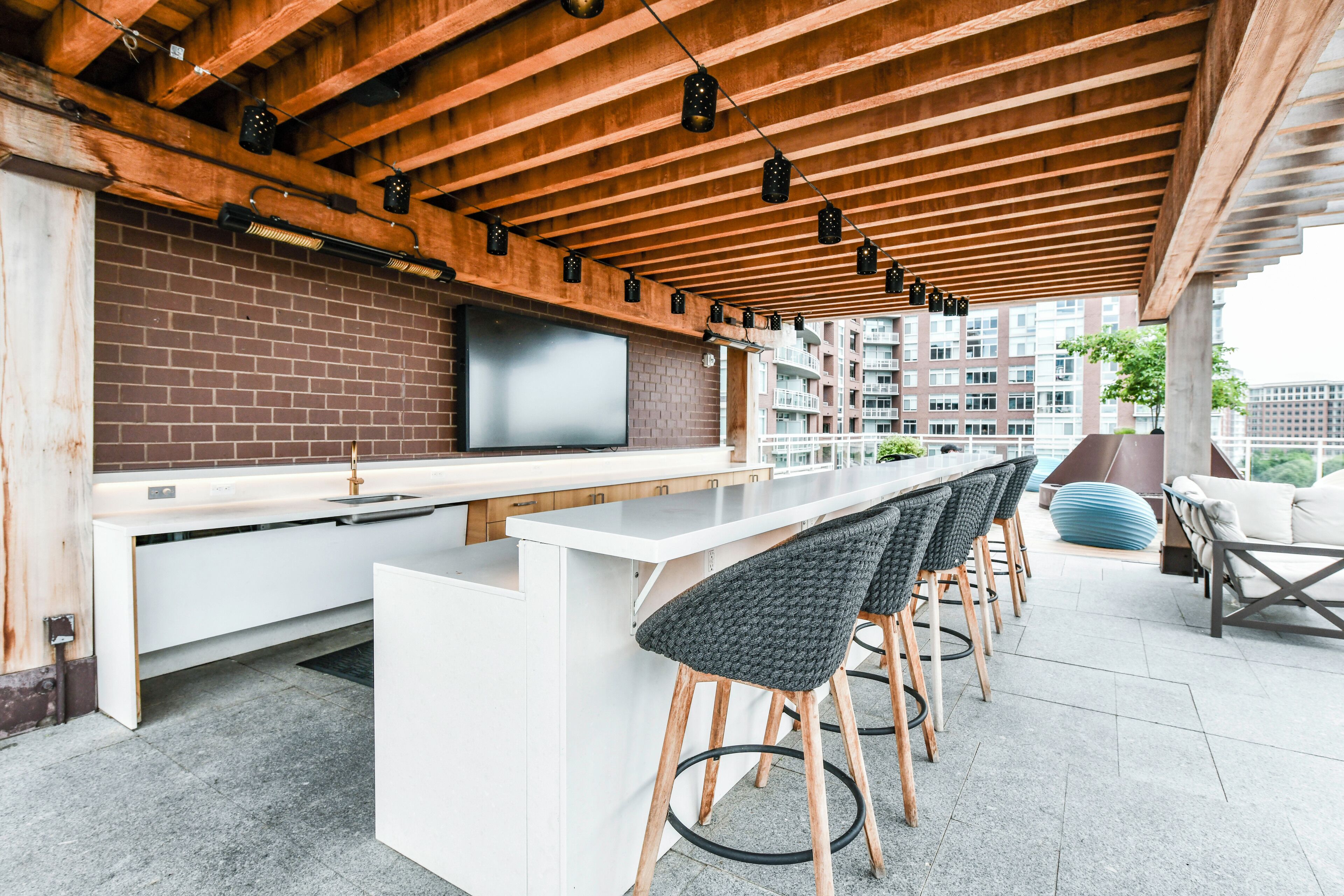 An outdoor bar area with a white countertop, black bar stools, and a brick wall.