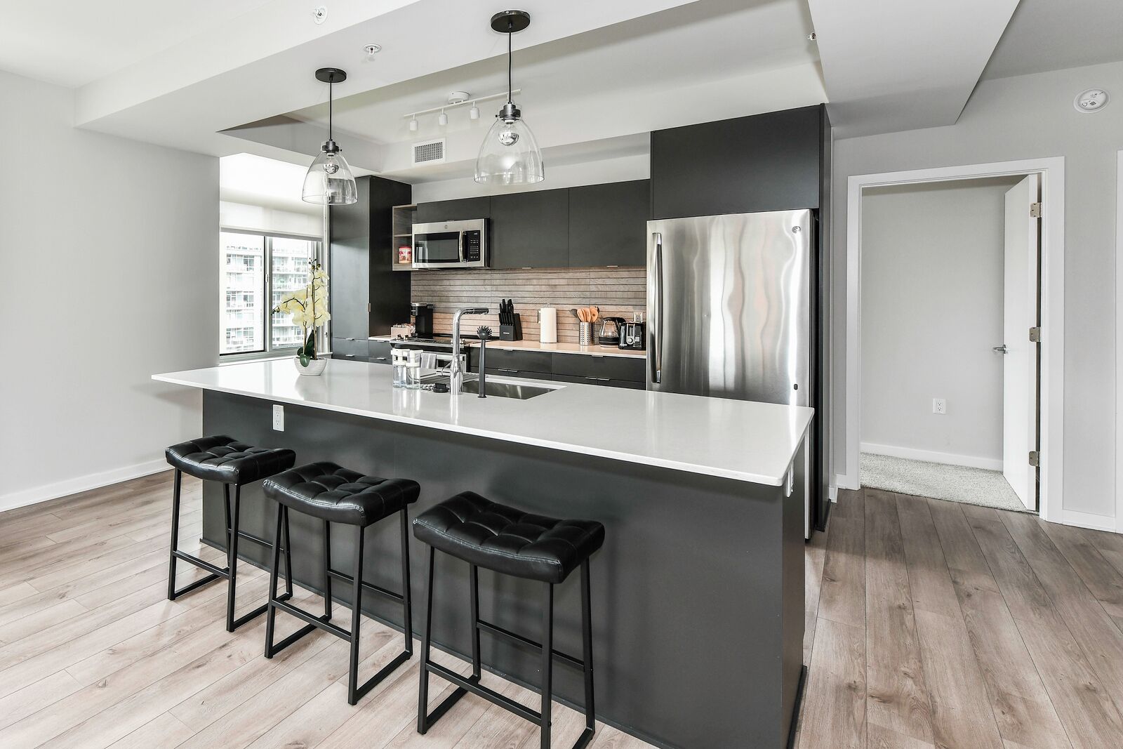 Een moderne keuken met een centraal eiland, roestvrijstalen apparatuur en zwarte barkrukken.