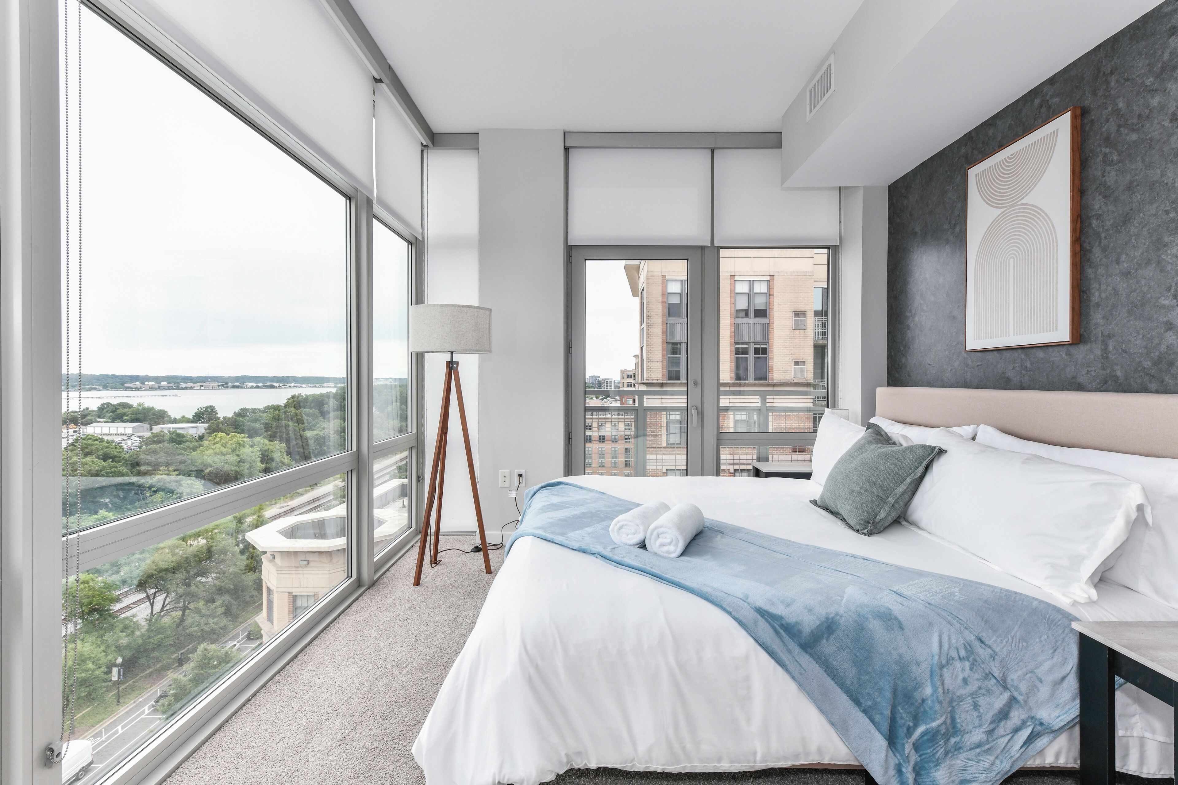 Une chambre d’hôtel moderne avec un grand lit, une vue sur la ville et une lampe sur pied.