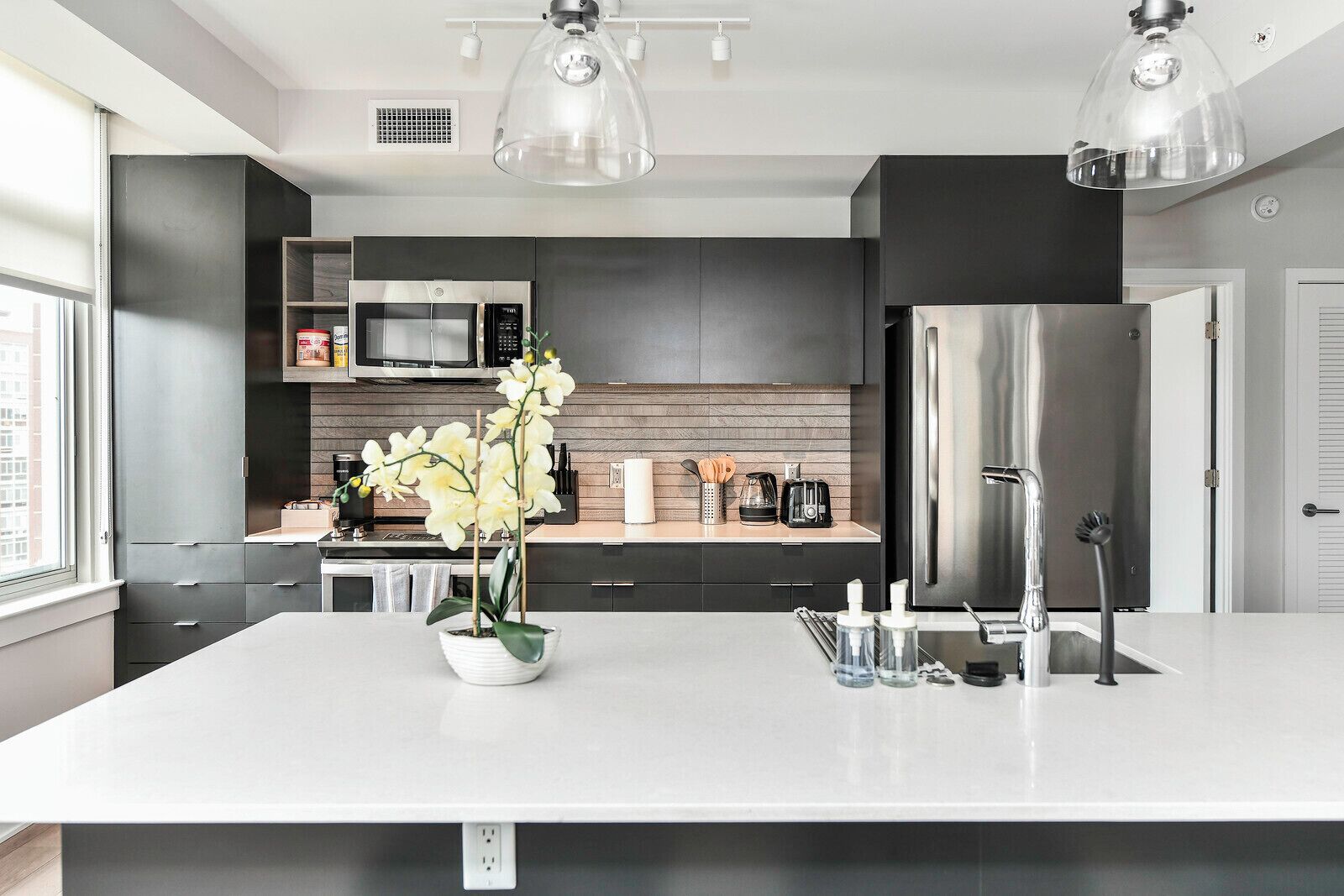 A modern kitchen with a large island, stainless steel appliances, and pendant lighting.