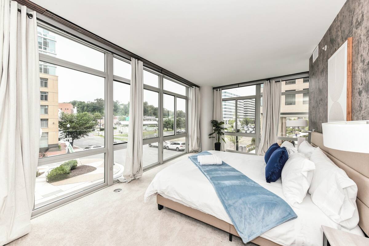Une chambre d’hôtel moderne dotée de grandes fenêtres, d’un lit, d’une table de chevet et offrant une vue sur la ville.