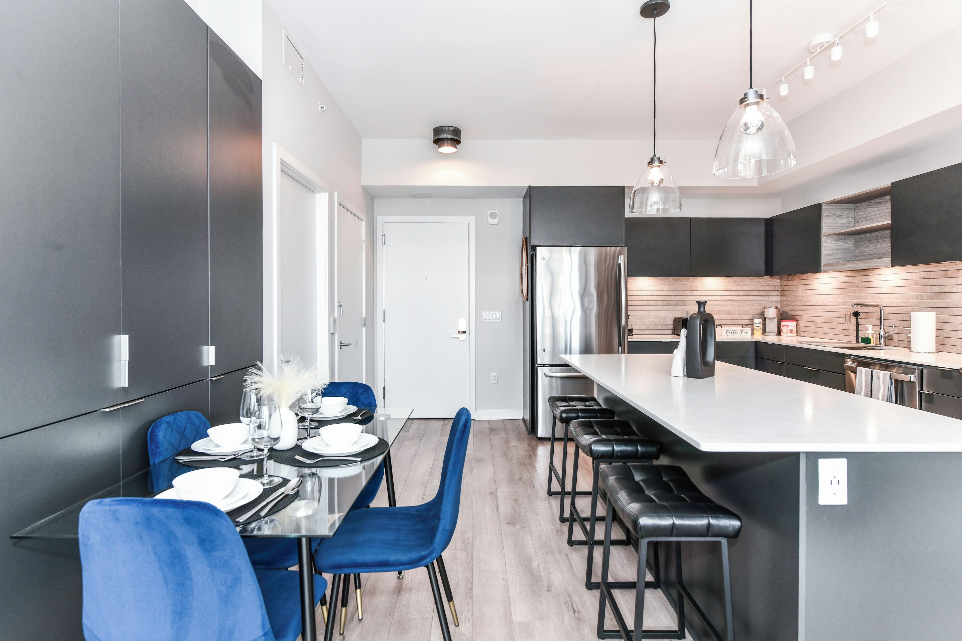 Una cocina moderna con una isla central, taburetes de bar y un comedor con sillas azules.