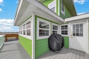 A green and white building with a covered grill, a wooden bench, and a view of the water. - The Happy Beach House (San Leon)