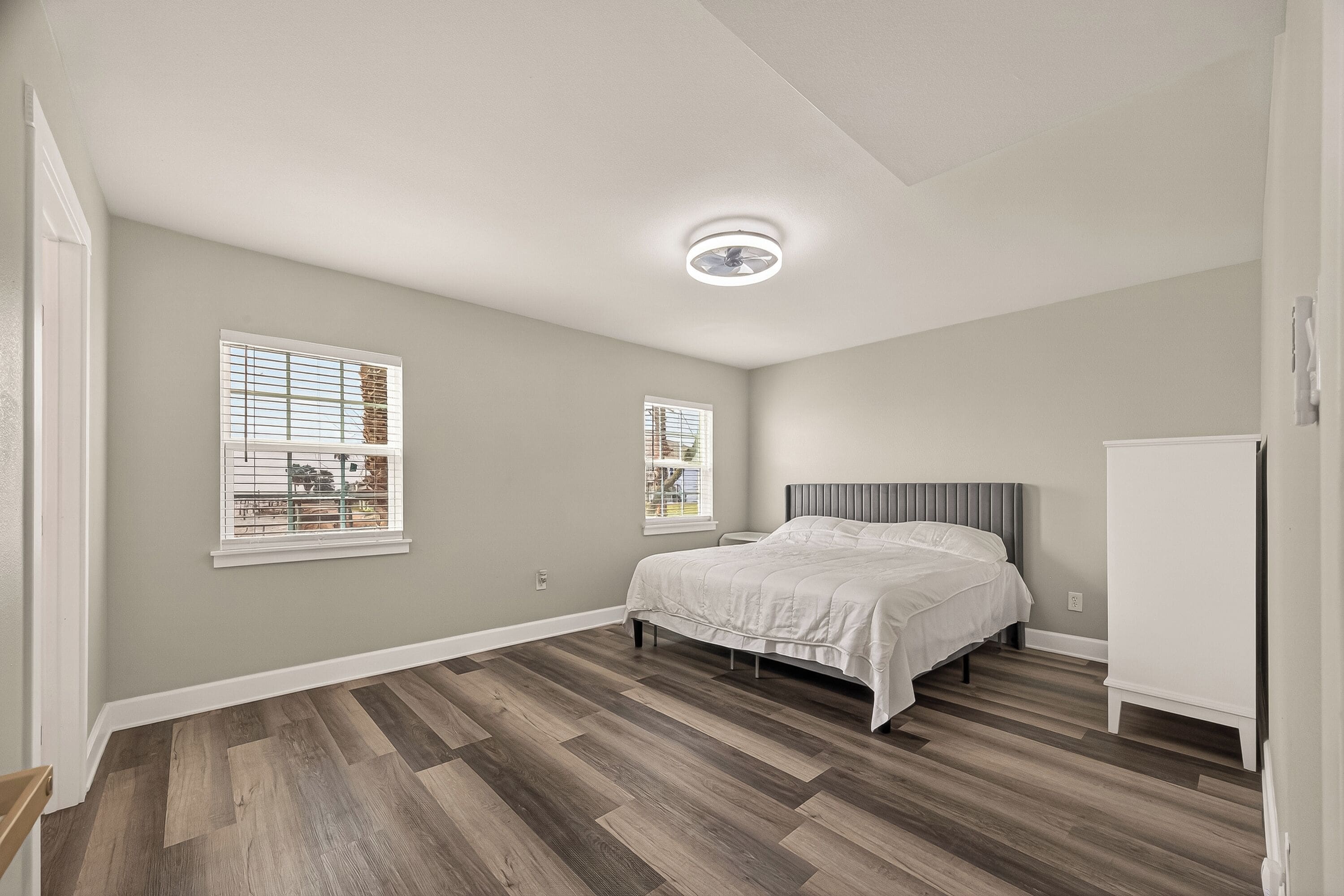 A bedroom with a bed, two windows, a ceiling fan, and a white wardrobe.