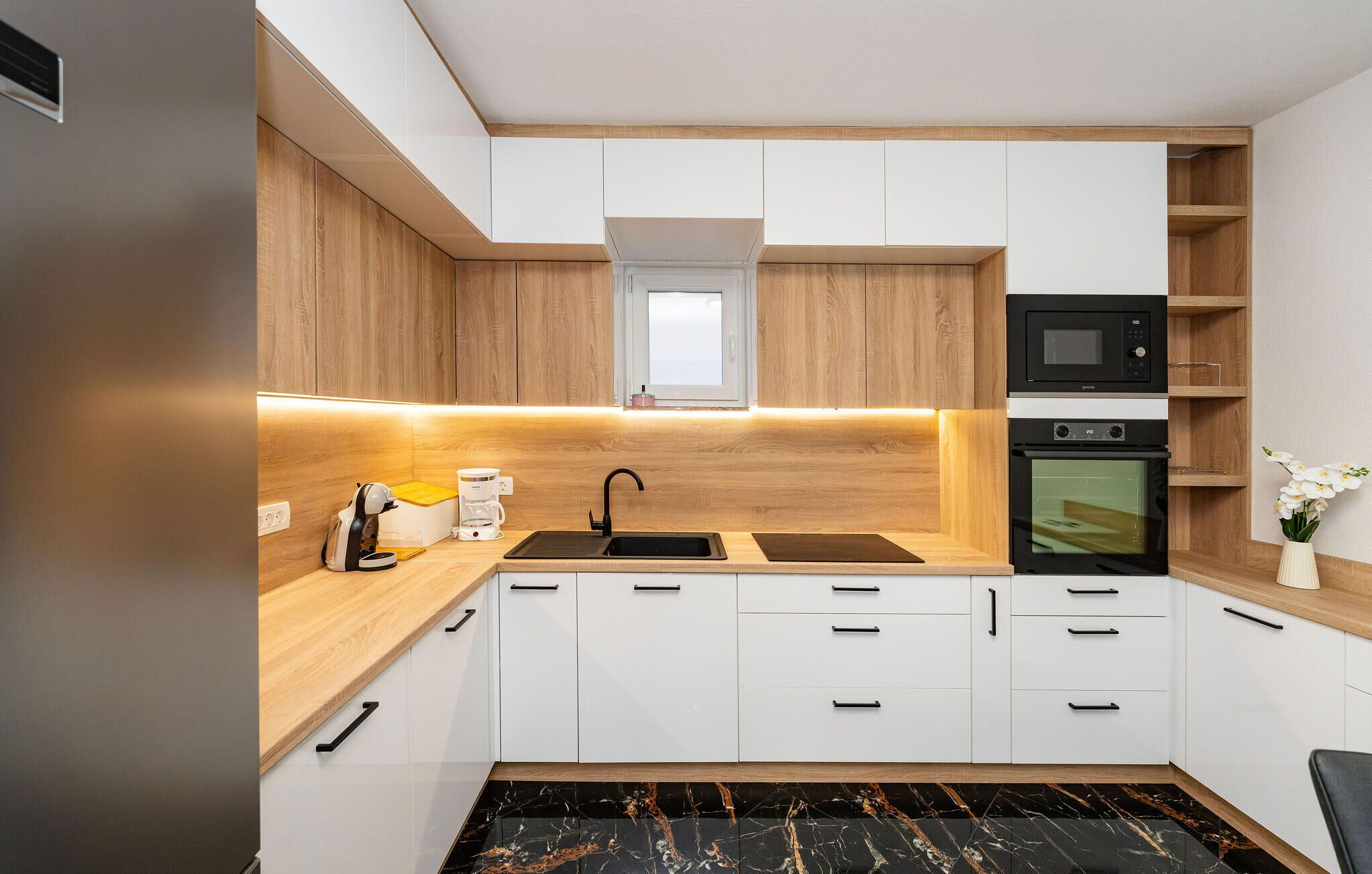 Une cuisine moderne avec des meubles blancs, un plan de travail noir, un four à micro-ondes encastré et un four traditionnel.