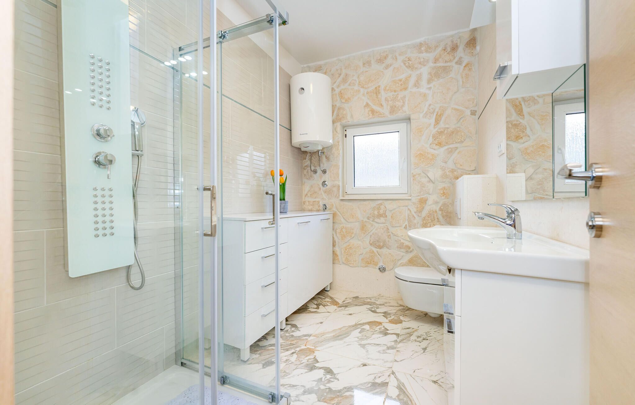 A modern bathroom with a glass-enclosed shower, a white sink, and a stone-patterned wall.