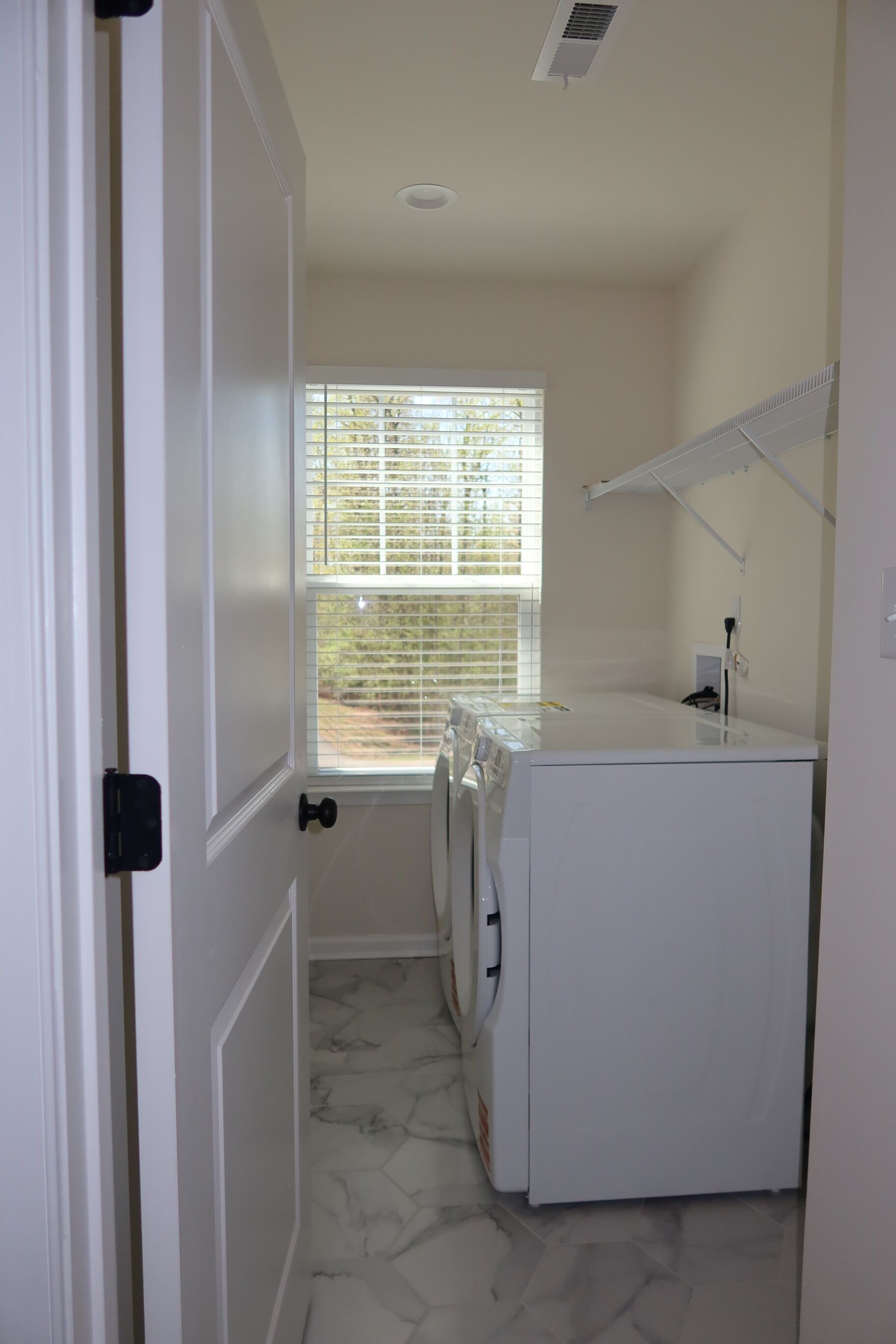 A laundry room with a washing machine, dryer, and a window with blinds.