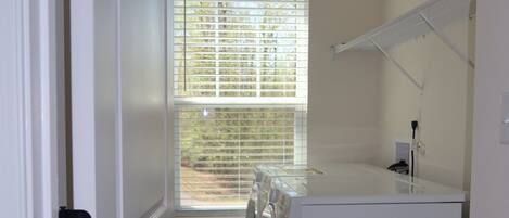 A laundry room with a washing machine, dryer, and a window with blinds.