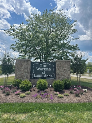 A sign for 'The Waters at Lake Anna' with a stone wall, a large tree, and landscaped flower beds.