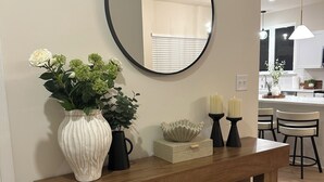 Una sala moderna con una consola de madera, un espejo redondo y objetos decorativos.