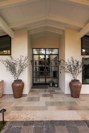 A building entrance with a covered porch, two large potted plants, and a glass door leading inside. - La Jolla Luxury | Designer Home w/ Pool & Jacuzzi! (San Diego)