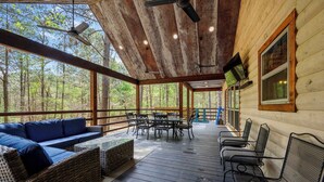 A covered outdoor area with a wooden deck, wicker furniture, and metal chairs. - Drift Inn, amazing back yard privacy! hot tub (Broken Bow)