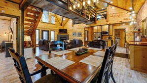 A wooden cabin interior with a dining table, chairs, a fireplace, and a kitchen area. - Drift Inn, amazing back yard privacy! hot tub (Broken Bow)