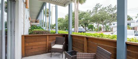 Un espacio de estar al aire libre cubierto, con muebles de mimbre y vista a la calle.