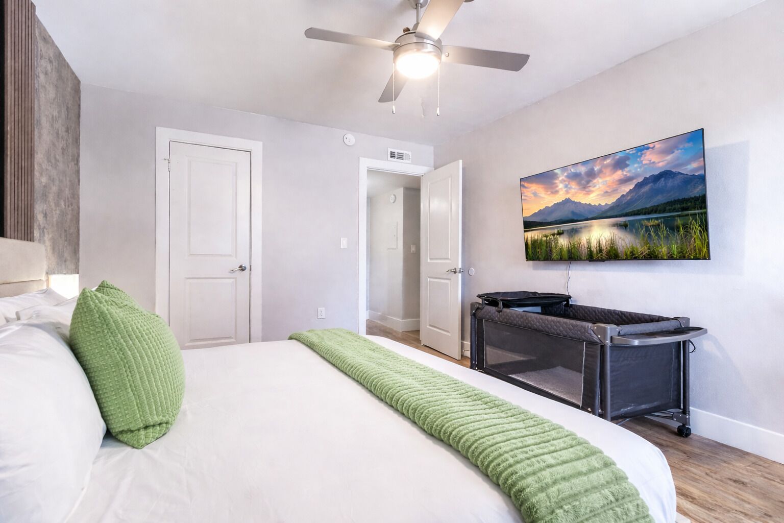 Un dormitorio con cama, ventilador de techo, un cuadro de paisaje y un carrito pequeño.