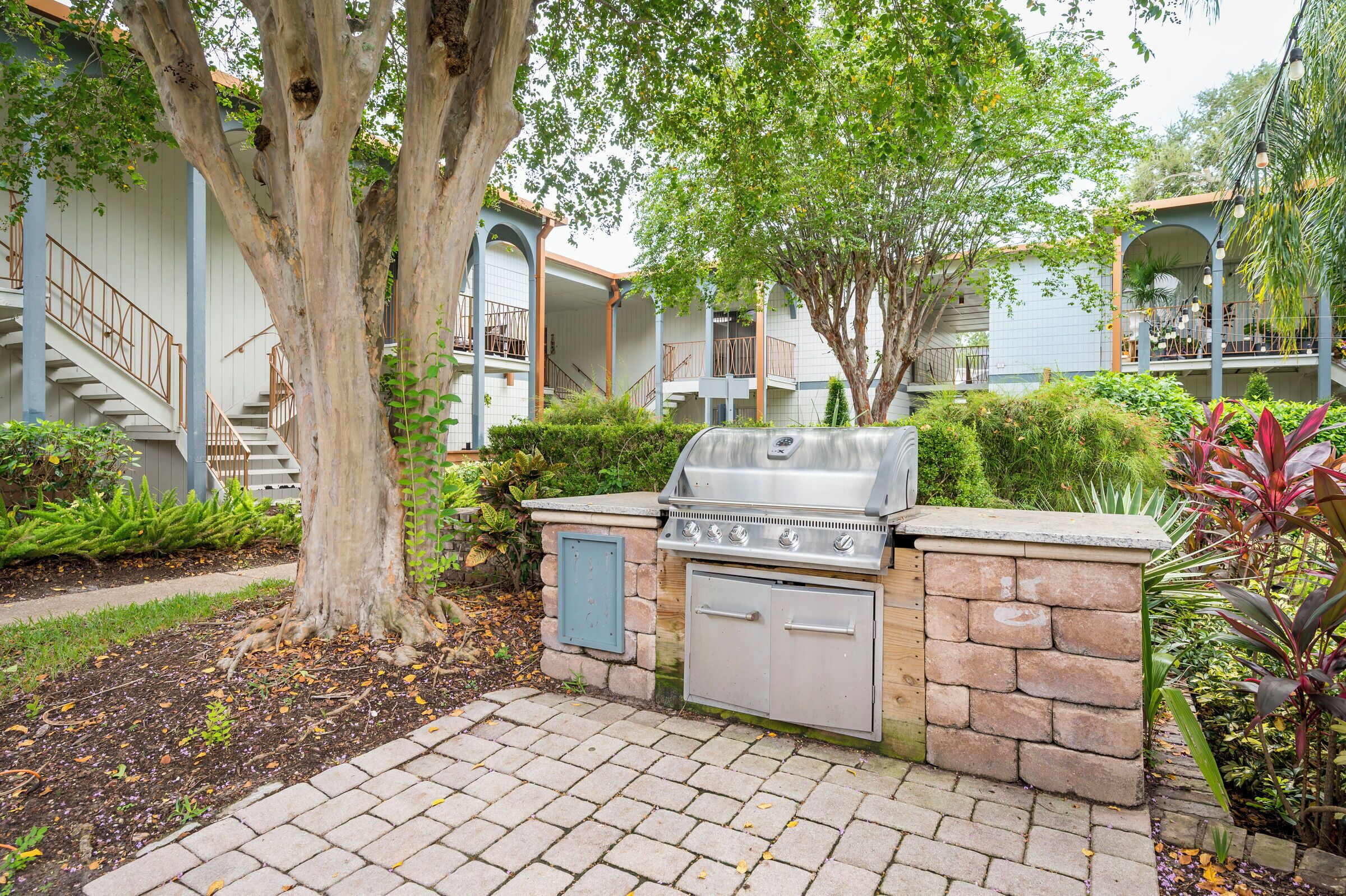 Un espace barbecue extérieur avec des murs en pierre, un escalier et un jardin agrémenté de différentes plantes.