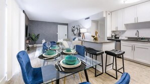 A modern kitchen with white cabinets, a central island, and a dining area with a glass table and blue chairs.